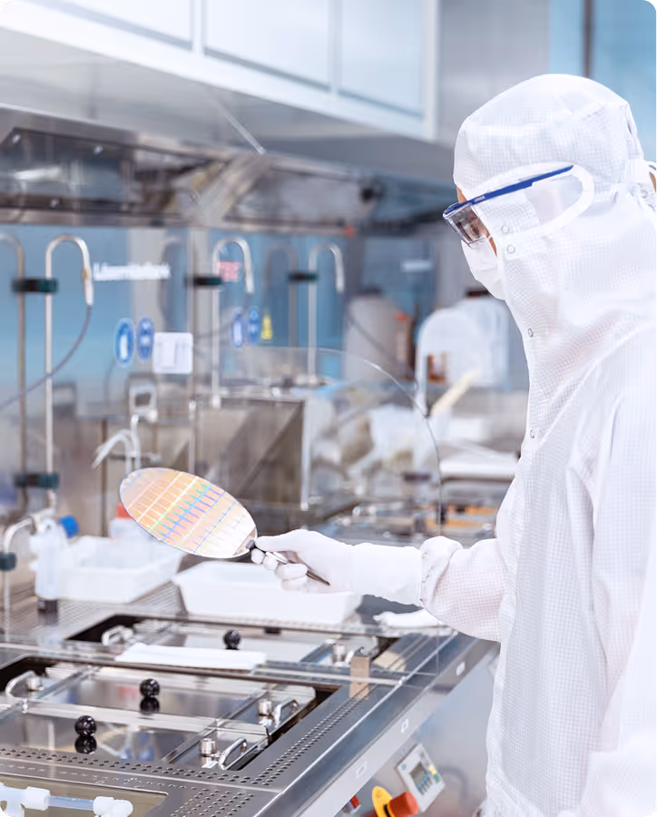 Scientist in cleanroom suit inspecting a silicon wafer in a high-tech semiconductor fabrication lab.