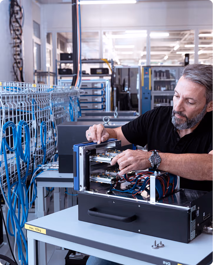 Technician assembling or repairing electronic components inside a device in a modern laboratory or workshop with blue cables and equipment in the background.