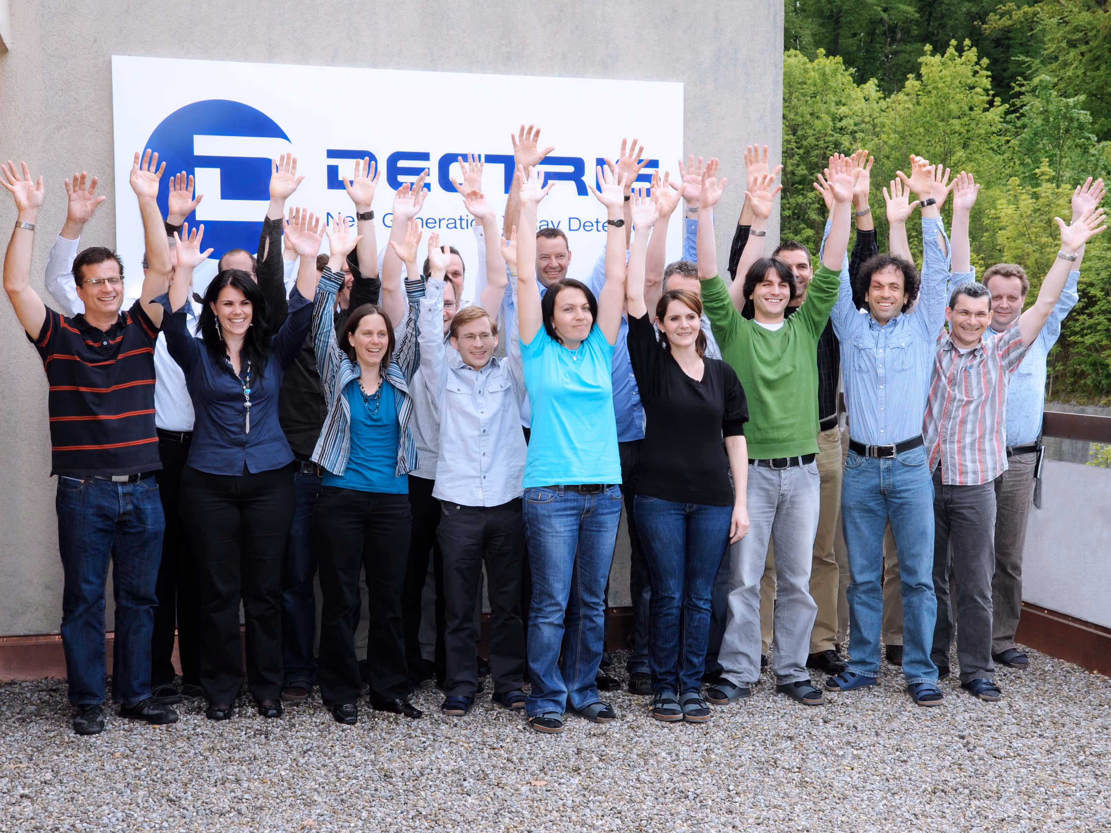 Group of people standing outdoors with arms raised in front of a DETRIX sign on a wall.