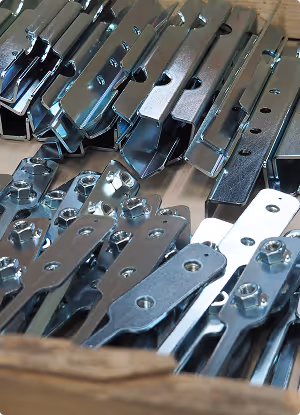 Metal hardware pieces with holes and bolts stacked in a wooden crate.