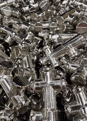 Pile of shiny metal crosses with some having engraved lines on a reflective surface.