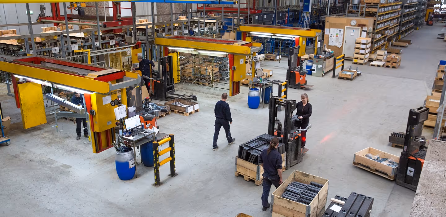 Warehouse interior with workers operating forklifts and assembling machinery parts on pallets.