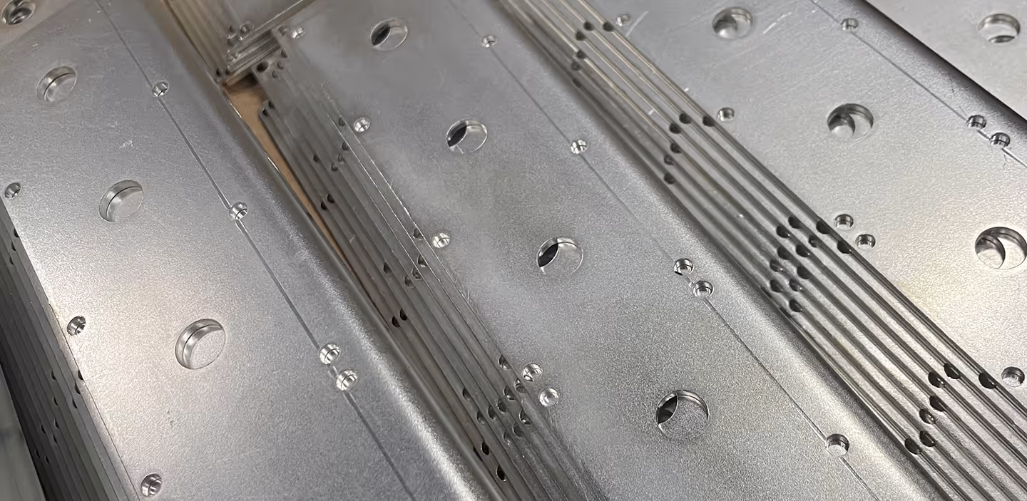 Stacked shiny metal plates with rounded holes punched in regular rows.