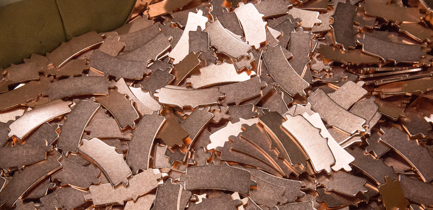 Pile of small, shiny copper-colored metal parts with irregular shapes and cutouts.