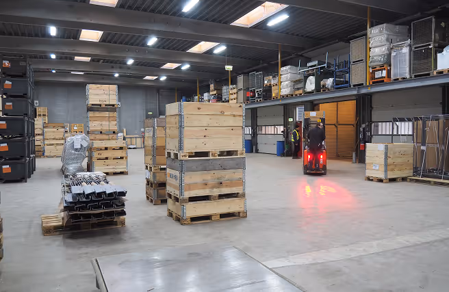 Warehouse interior with stacked wooden crates and a worker operating a forklift truck.
