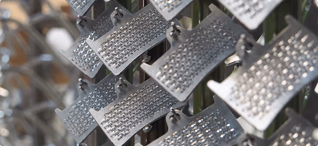 Close-up of metal grating sheets hanging in rows, showing detailed perforations and hooks.