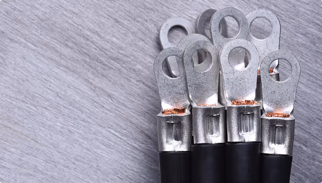 Close-up of six metal electrical cable lugs with black insulated wires on a gray surface.