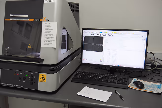 Scientific lab X-ray fluorescence analyzer next to computer displaying measurement data.