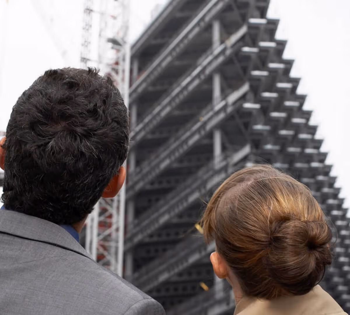 Two professionals in business attire looking up at a steel structure of a building under construction.