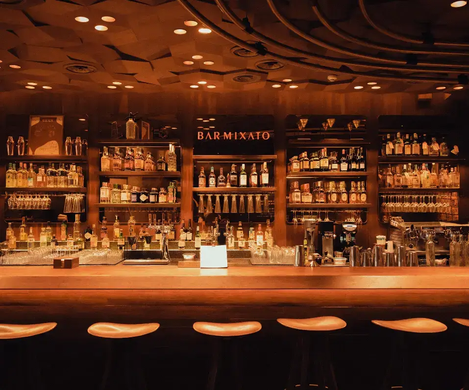 Comptoir de bar rétro éclairé avec alignement de bouteilles d'alcool pour l'organisation des Happy Hours.