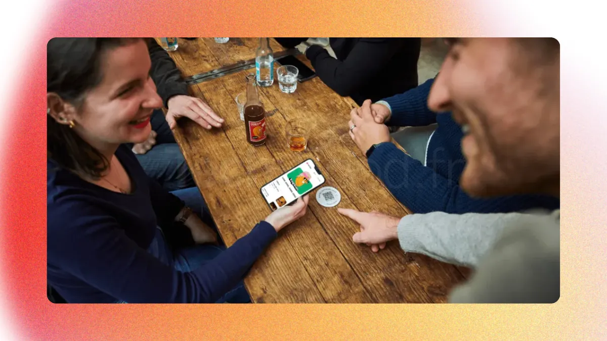 Scène de vie en restaurant où un serveur souriant montre du doigt le chevalet QR Code Sunday posé sur la table à une cliente. La cliente tient son smartphone en main, prête à scanner le code pour régler son addition en toute autonomie.