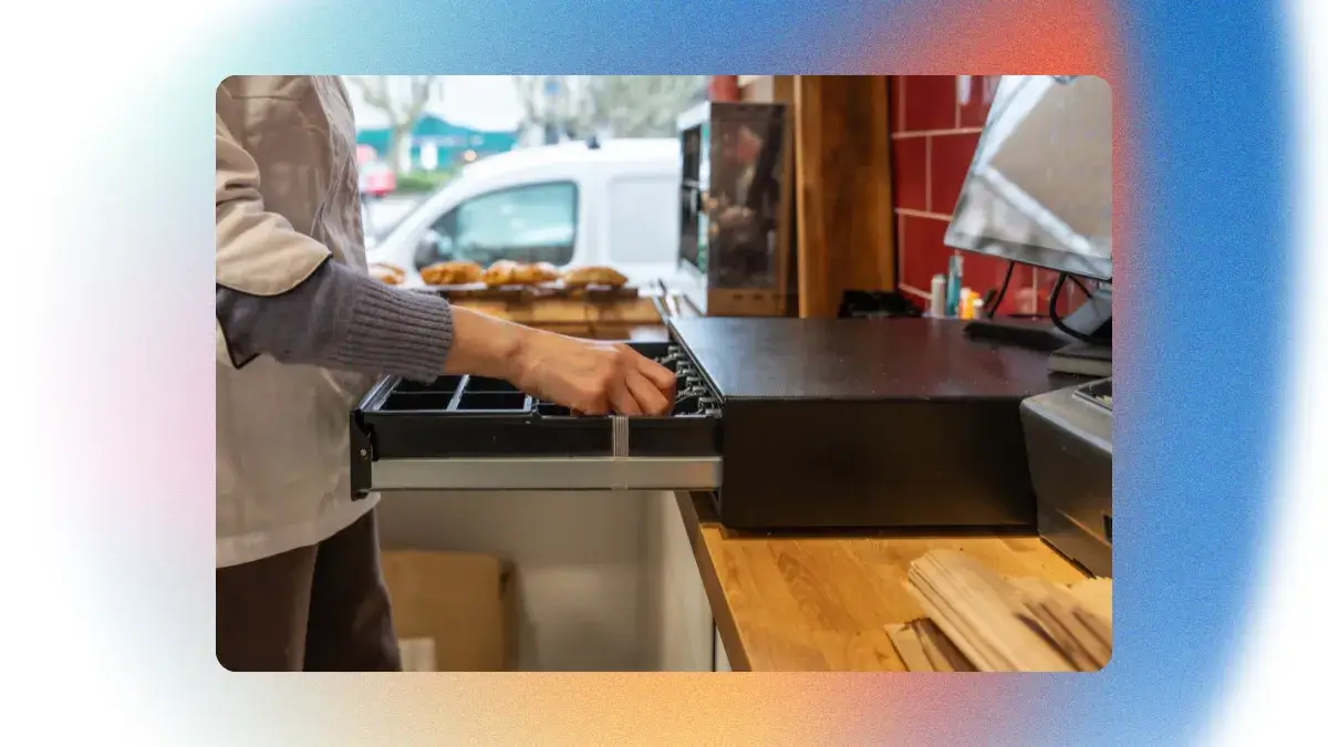 Gros plan sur un tiroir-caisse en acier ouvert contenant des pièces et des billets au comptoir d'un restaurant.
