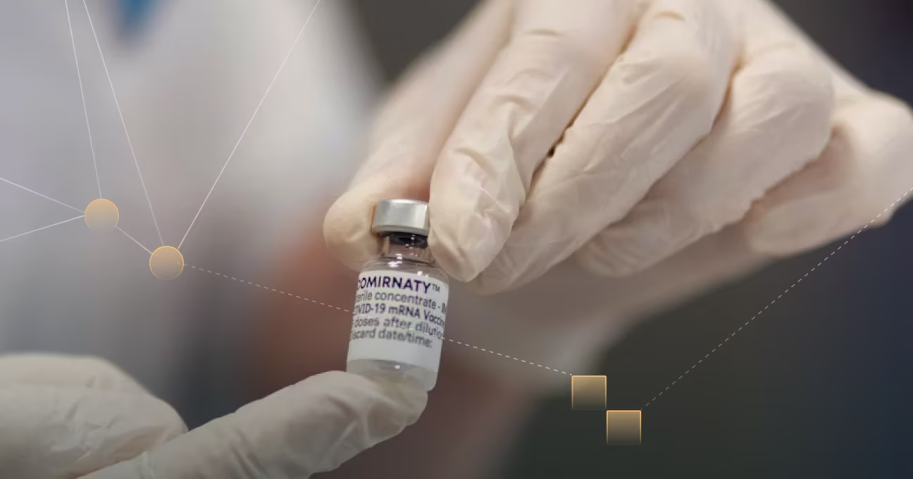 Gloved hands holding a small vial vaccine.