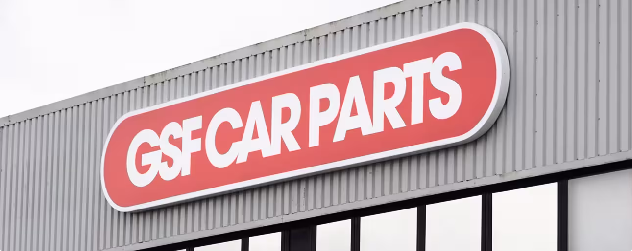 Red and white sign reading 'GSF CAR PARTS' on a gray corrugated building wall.