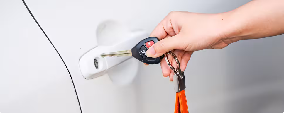 Hand holding a car key near a white vehicle's door handle ready to unlock it.