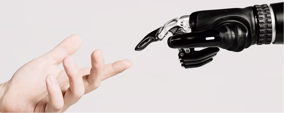Human hand reaching out to touch a robotic prosthetic hand against a plain background.