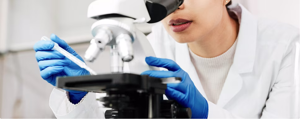 Scientist wearing blue gloves using a pipette to place a sample on a microscope slide.