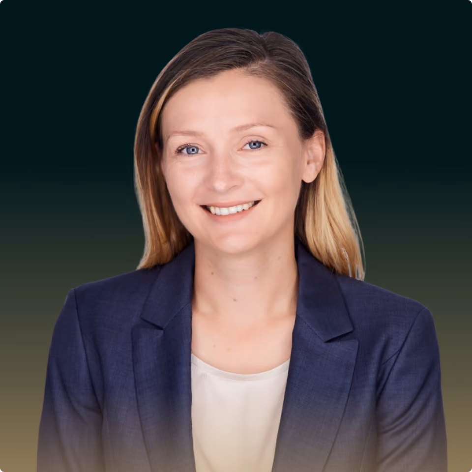 Smiling woman with blonde hair wearing a navy blazer and white top on a gradient dark background.