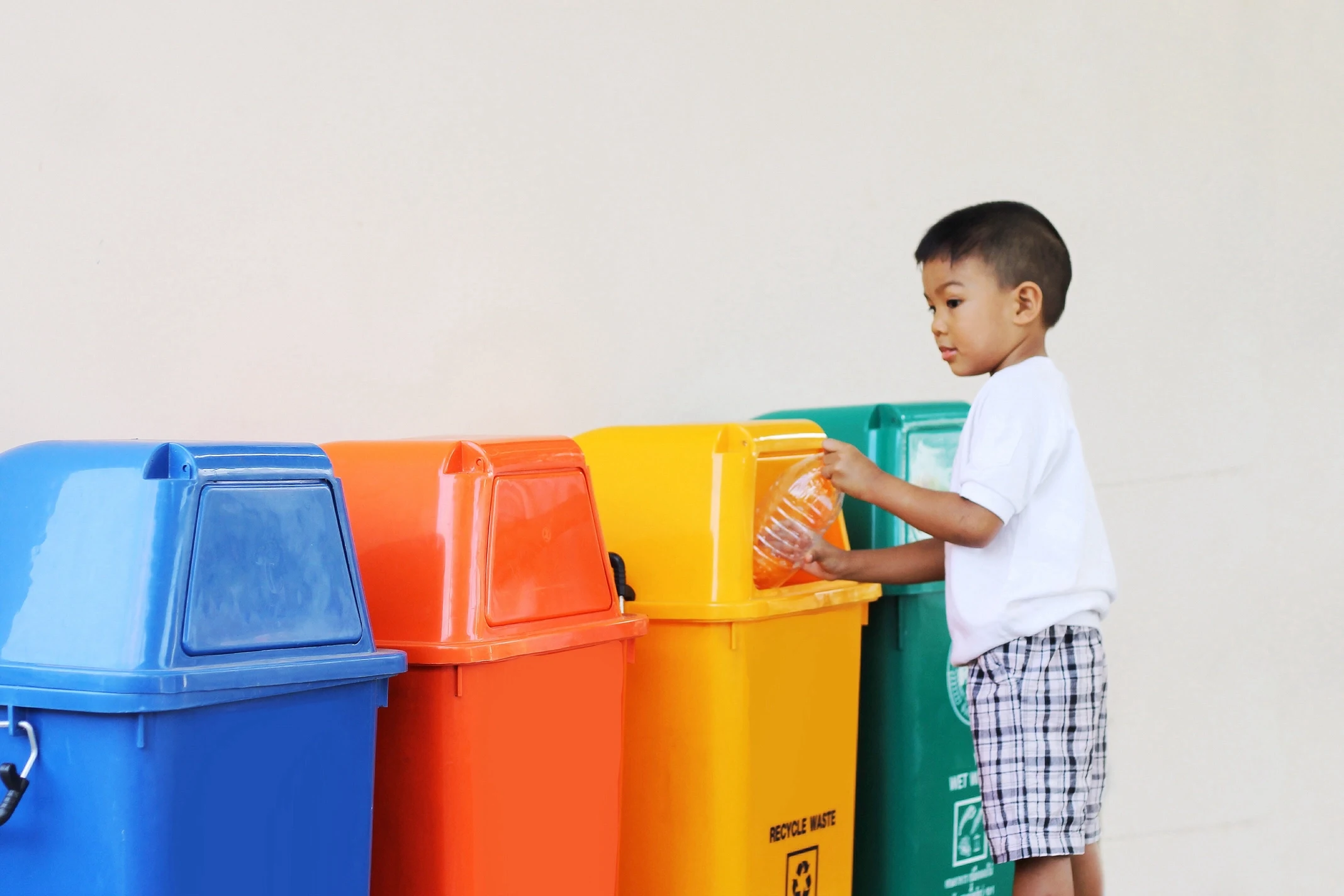 Child disposing of waste in one of four separated recycling bins to represent responsible waste management.