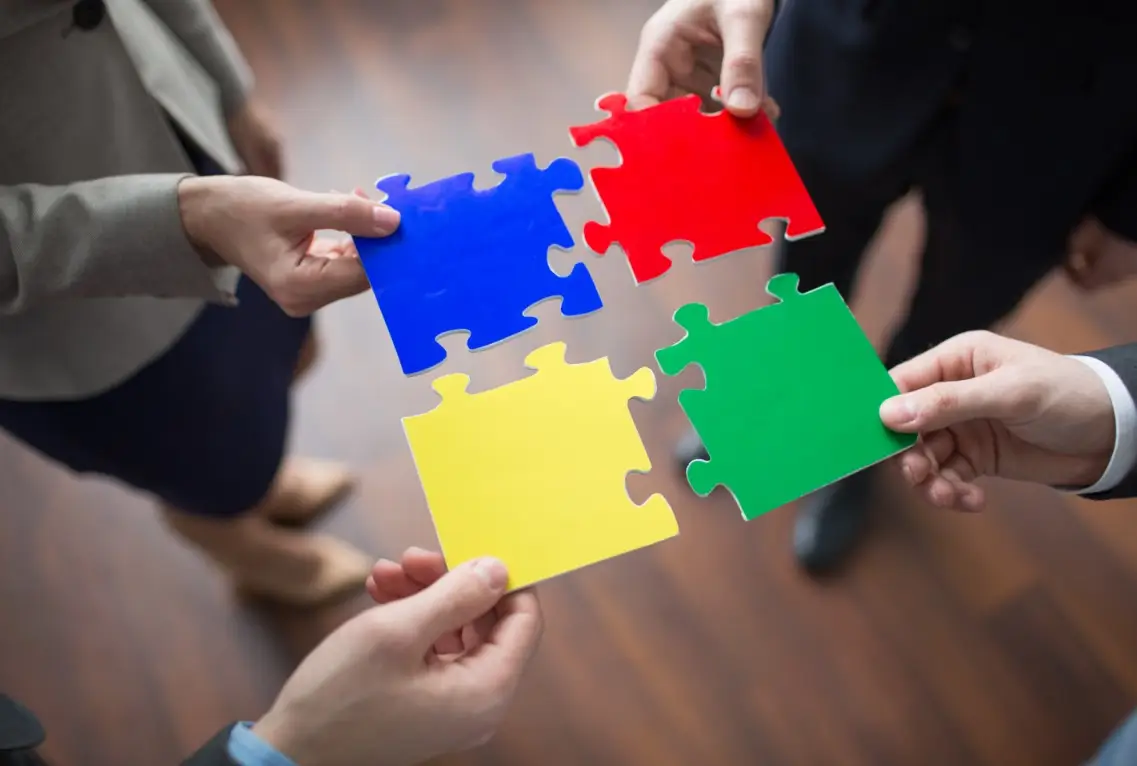four people connecting puzzle pieces to represent collaboration and the agile supply chain.