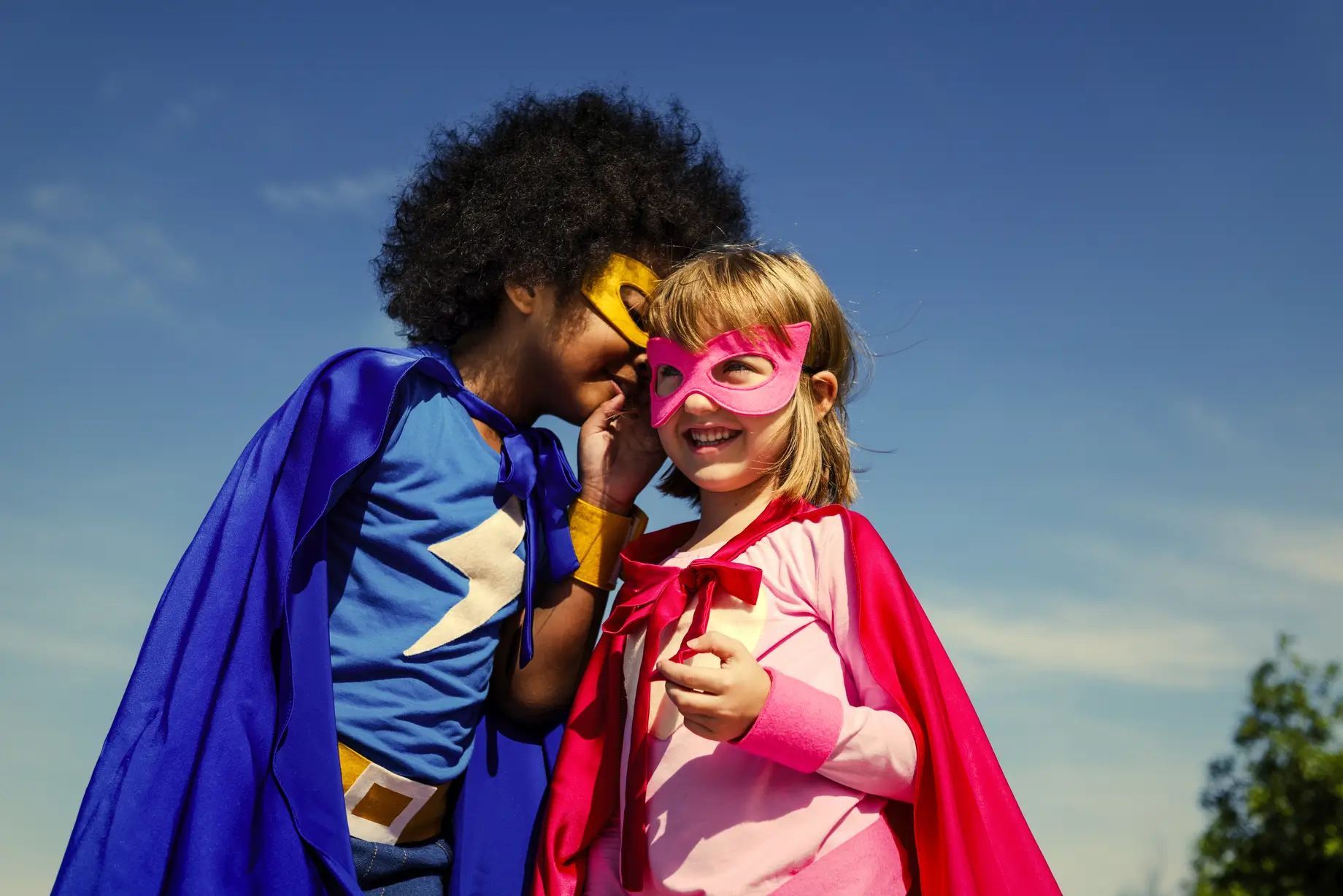 superhero boy whispering a secret for success into the ear of a small girl to represent tips for effective procurement negotiation.