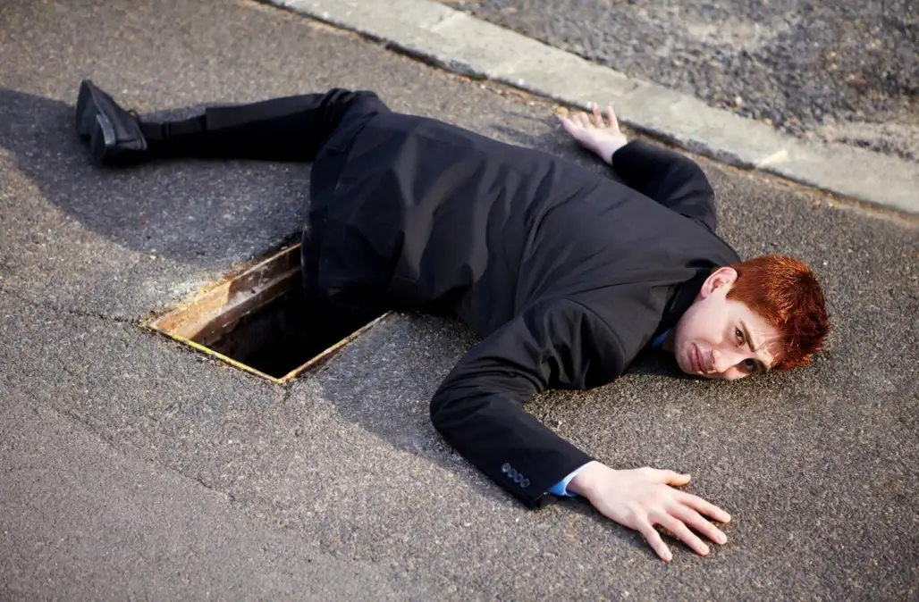 A man lying on ground with his leg in a pothole after he fell in by mistake
