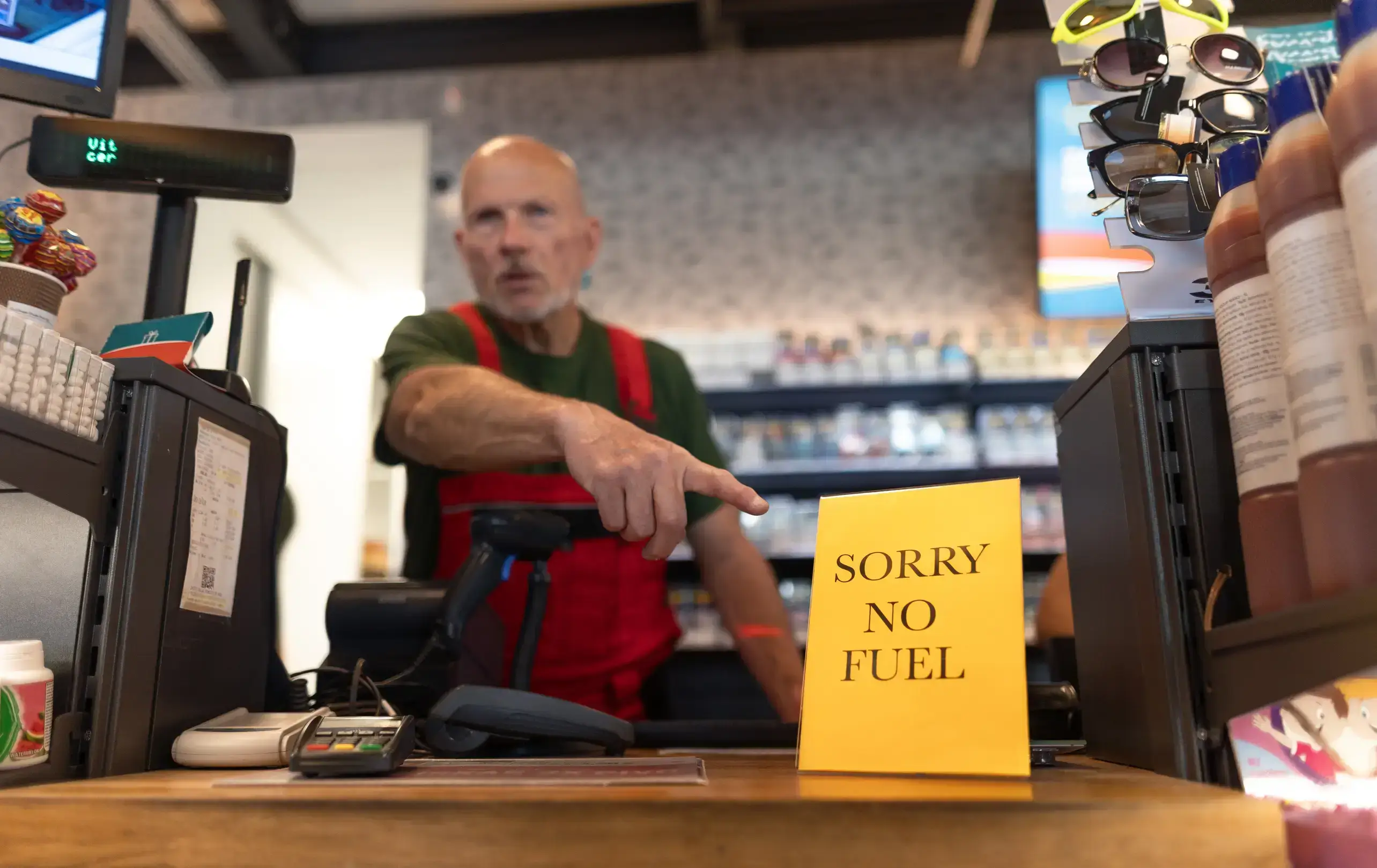 Store clerk pointing to a "no fuel" sign to represent the procurement risk of global energy price fluctuations
