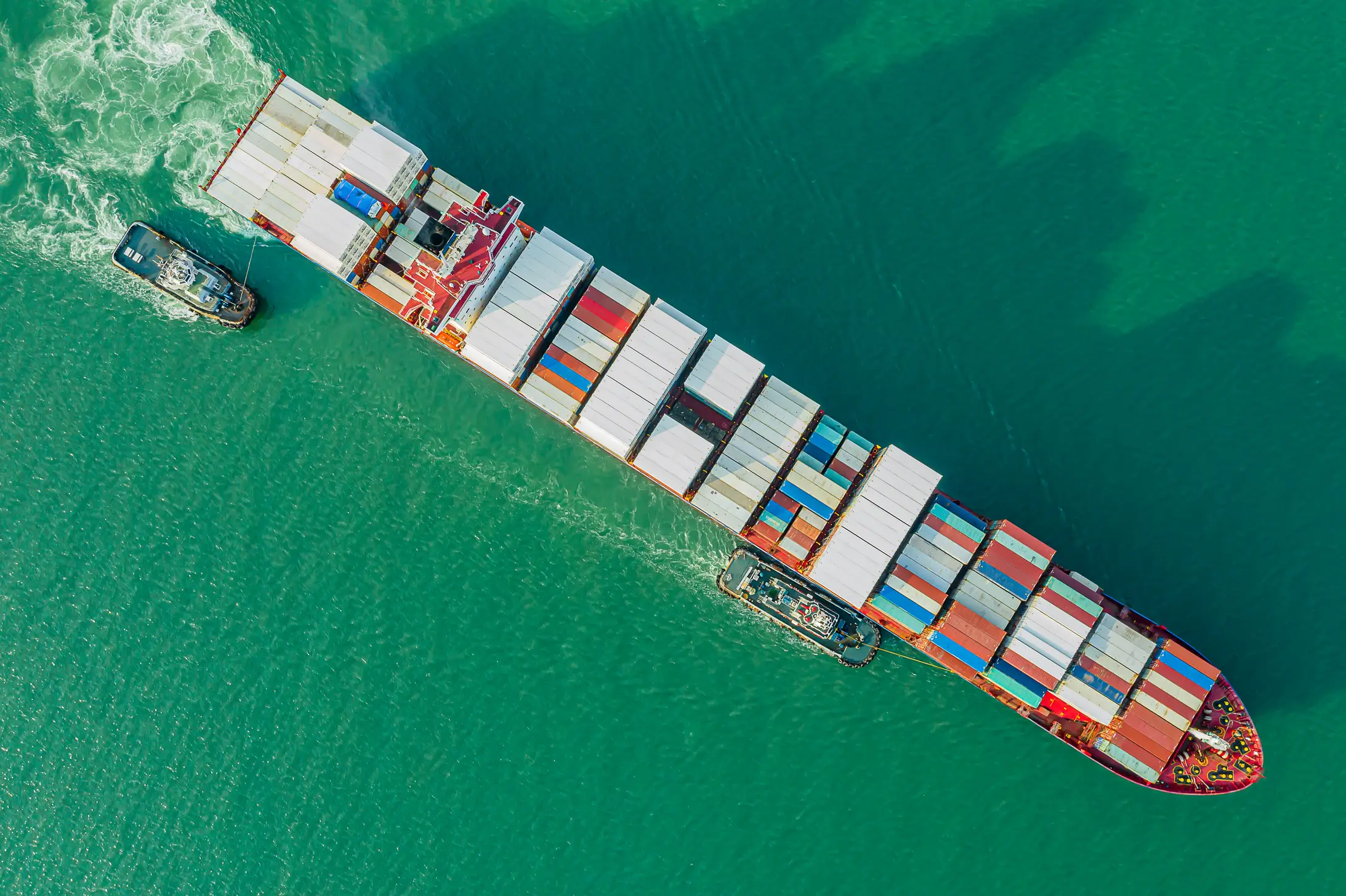 Cargo ship accompanied by two smaller boats to represent the importance of free passage through supply chain trade routes amidst geopolitical instability.