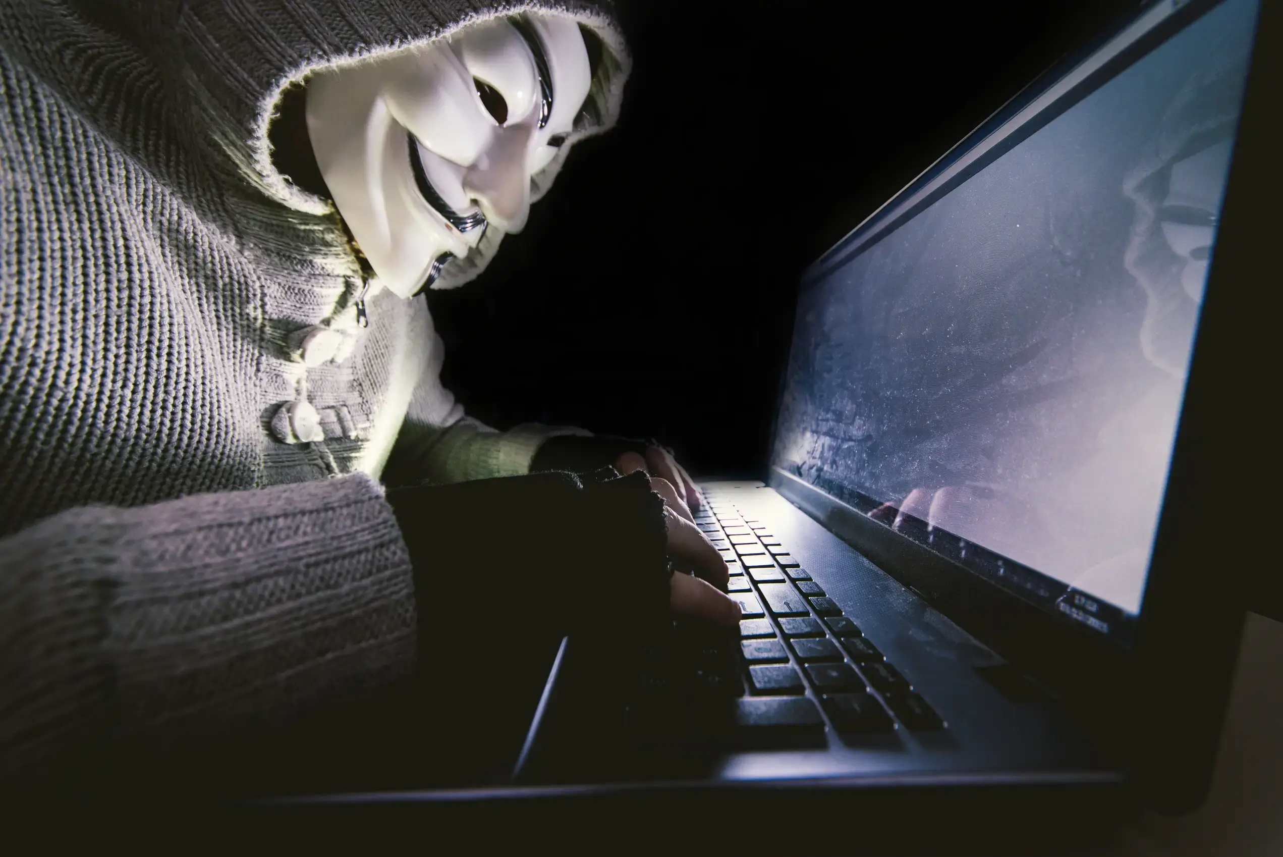 Masked cyber criminal hacking computer systems to represent rising cyber attacks and the need for strict data protection policies in supply chain risk management strategies.