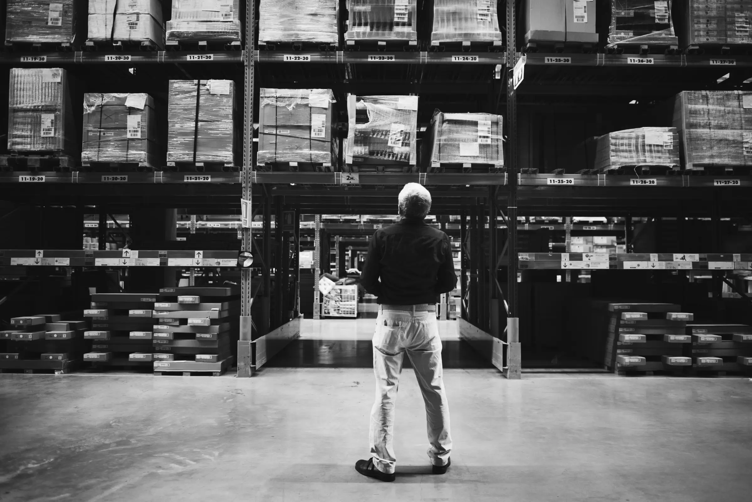 Man standing in front of a massive stock room full of inventory to represent the need to balance inventory with demand in procurement risk management.