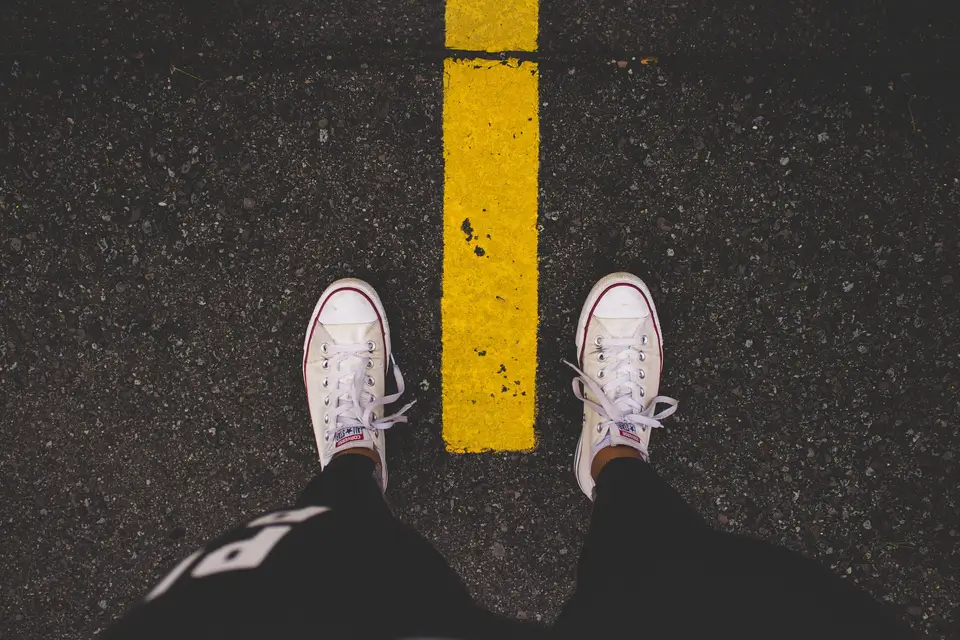 Person standing with each foot on a different side of a dividing line to represent the distinctions between purchasing and procurement.