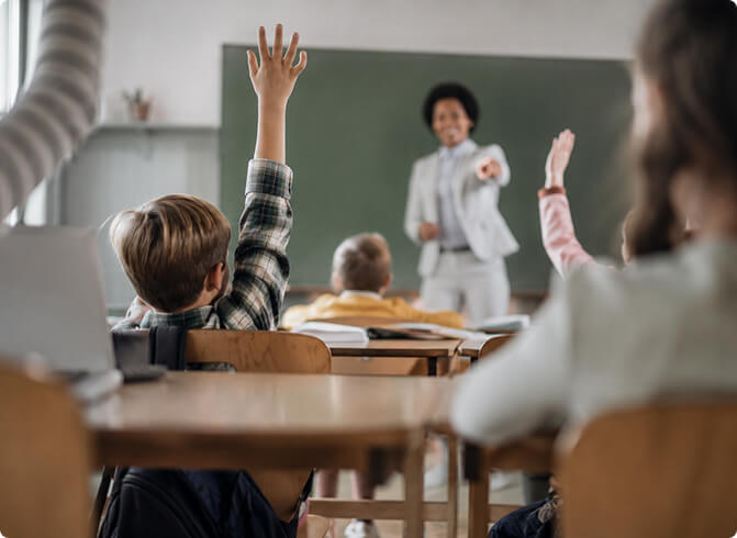 Teacher leading a classroom lesson while students raise their hands.