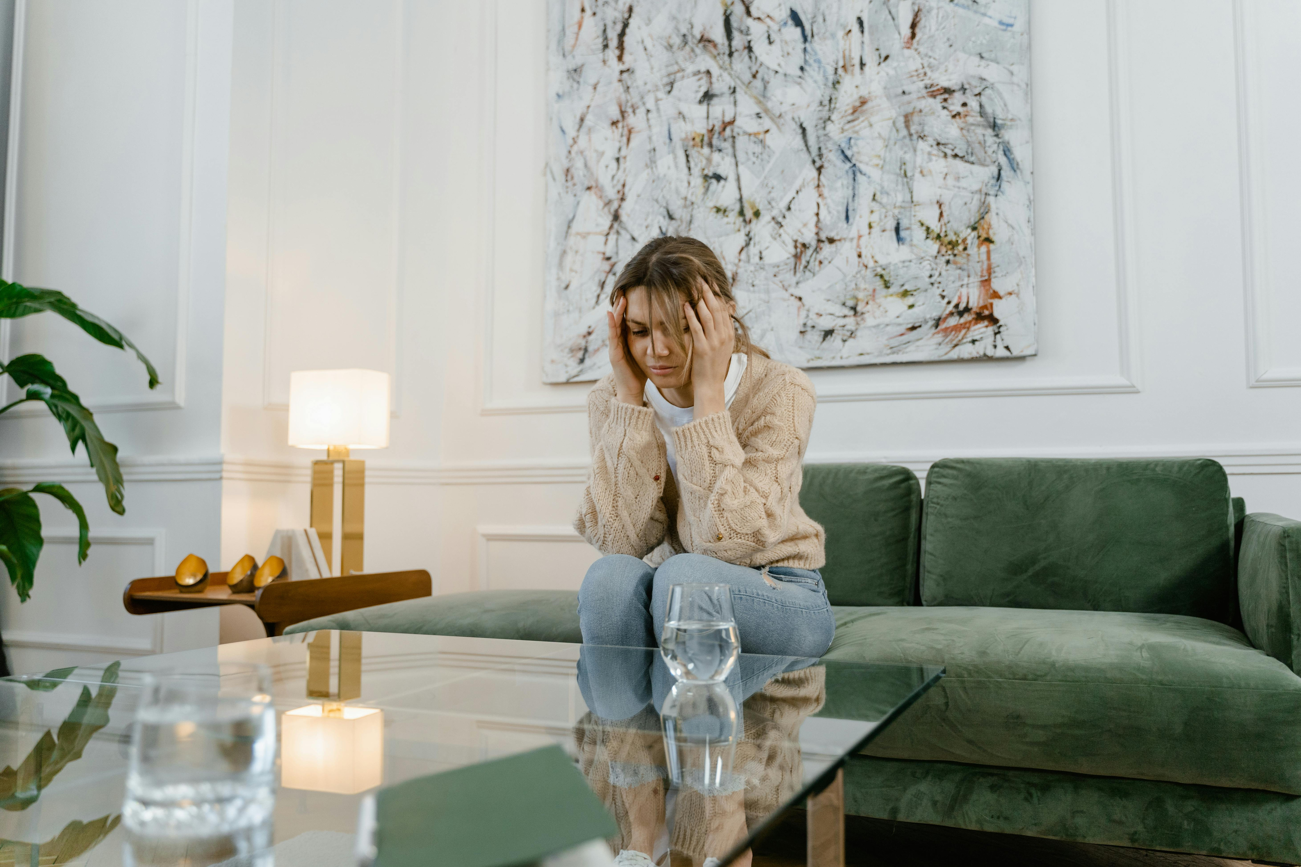Young woman sitting on a couch at home looking overwhelmed, reflecting the emotional weight of anxiety