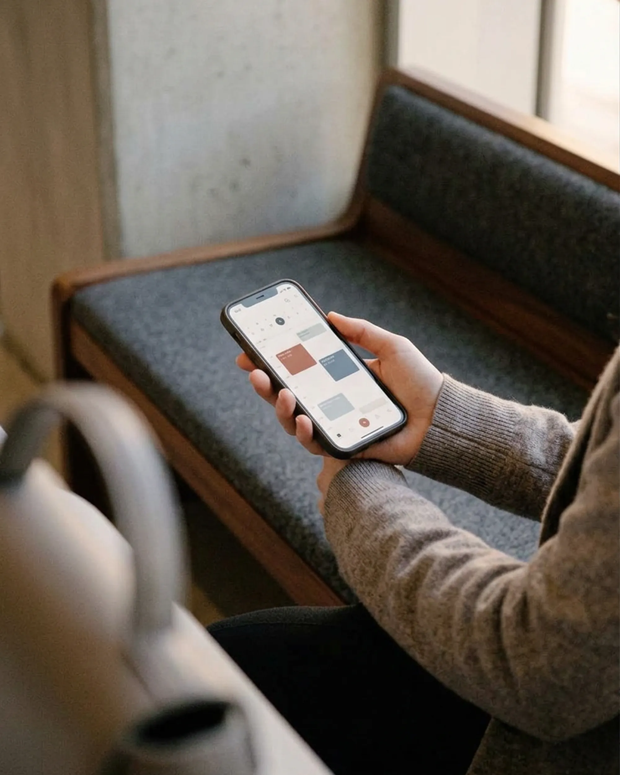 Person assise tenant un smartphone affichant un calendrier avec des événements colorés.
