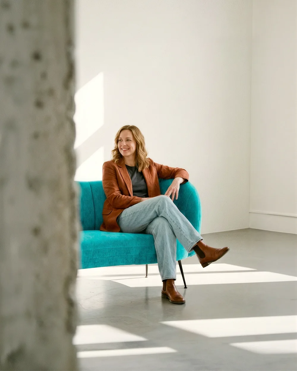 Une femme souriante assise sur un canapé bleu dans une pièce lumineuse aux murs blancs.