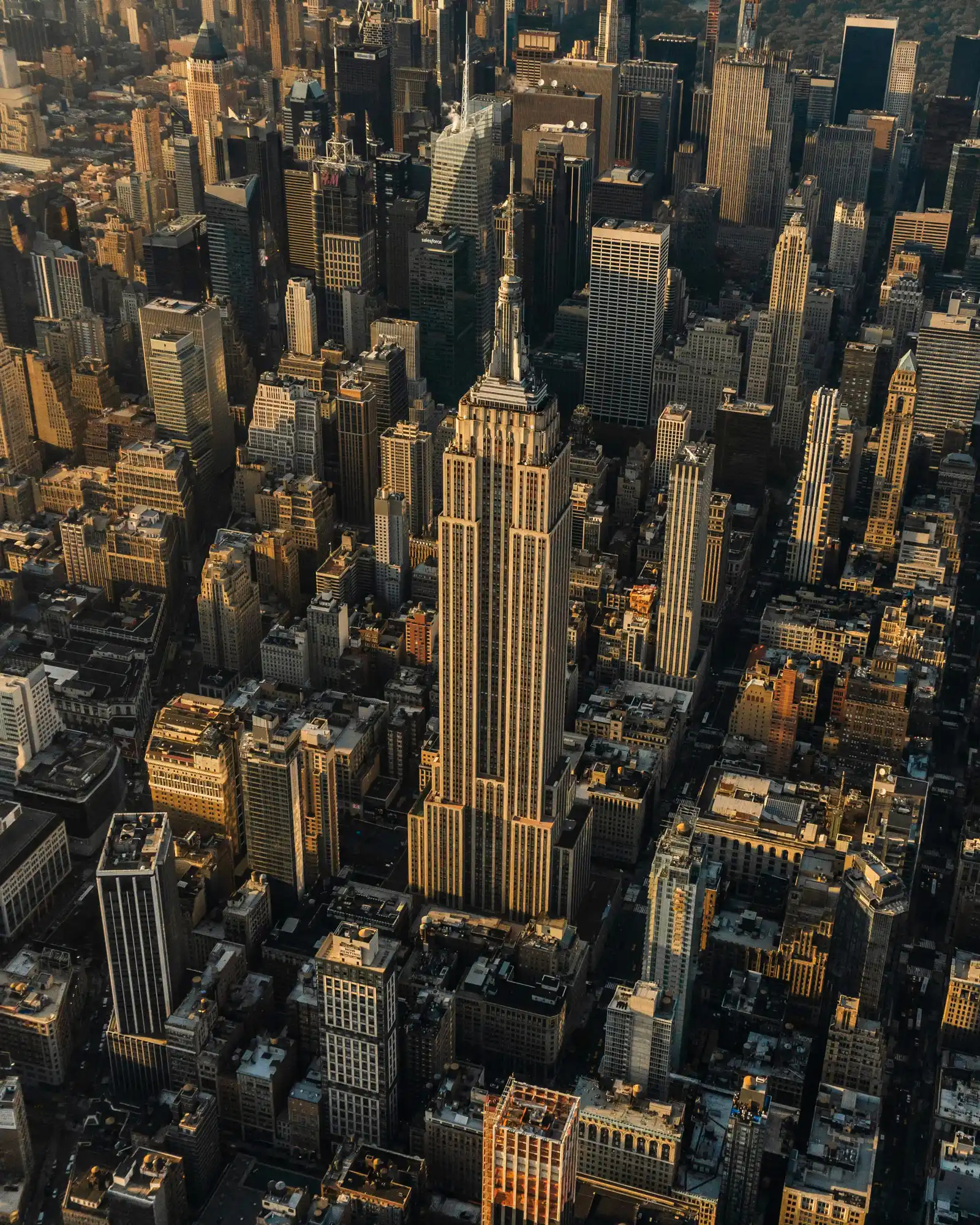 An aerial view of the New York City skyline at golden hour, centering on the Empire State Building surrounded by surrounding skyscrapers.