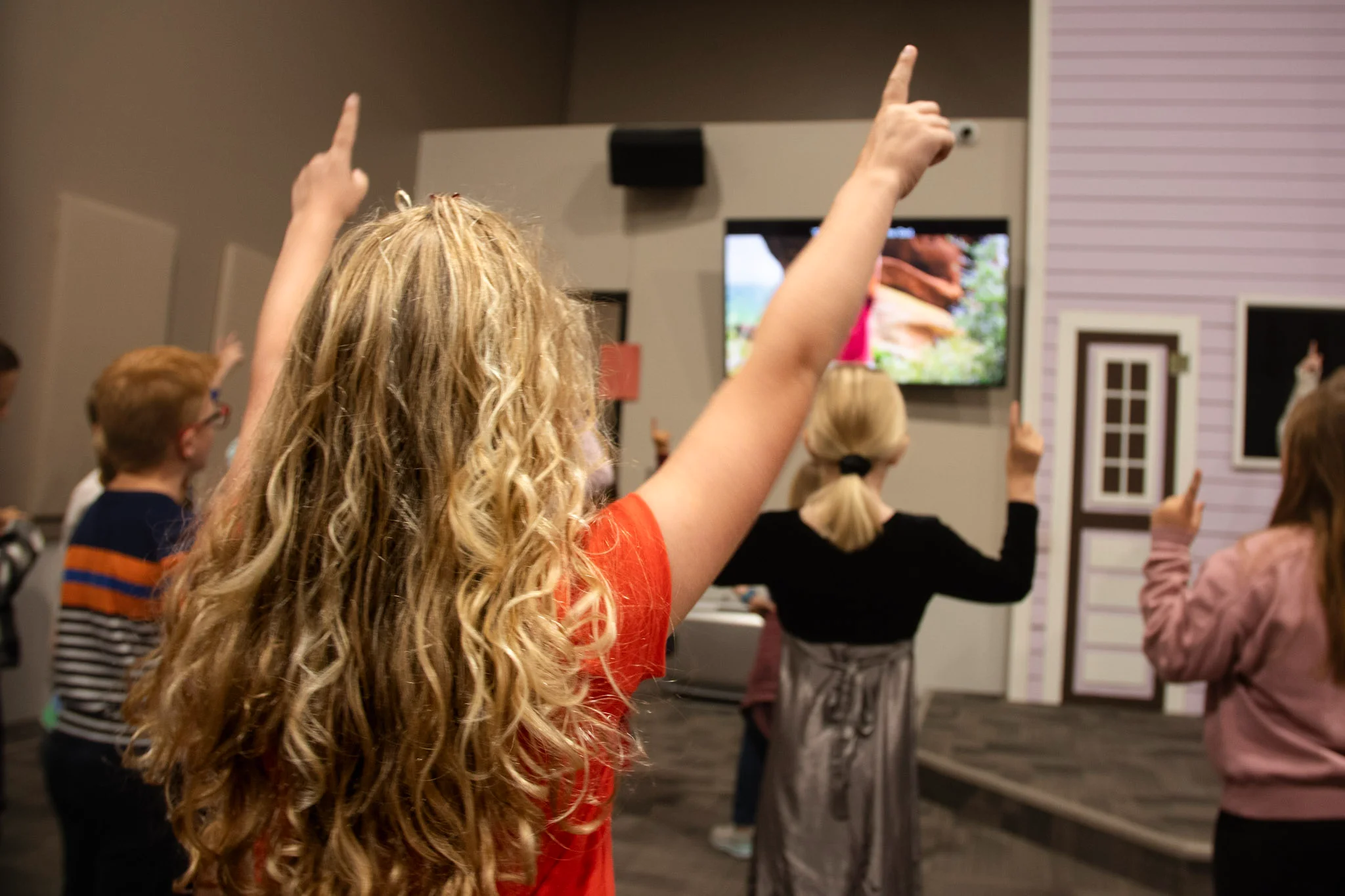 Children raising their hands during a kids church worship session inside a room.
