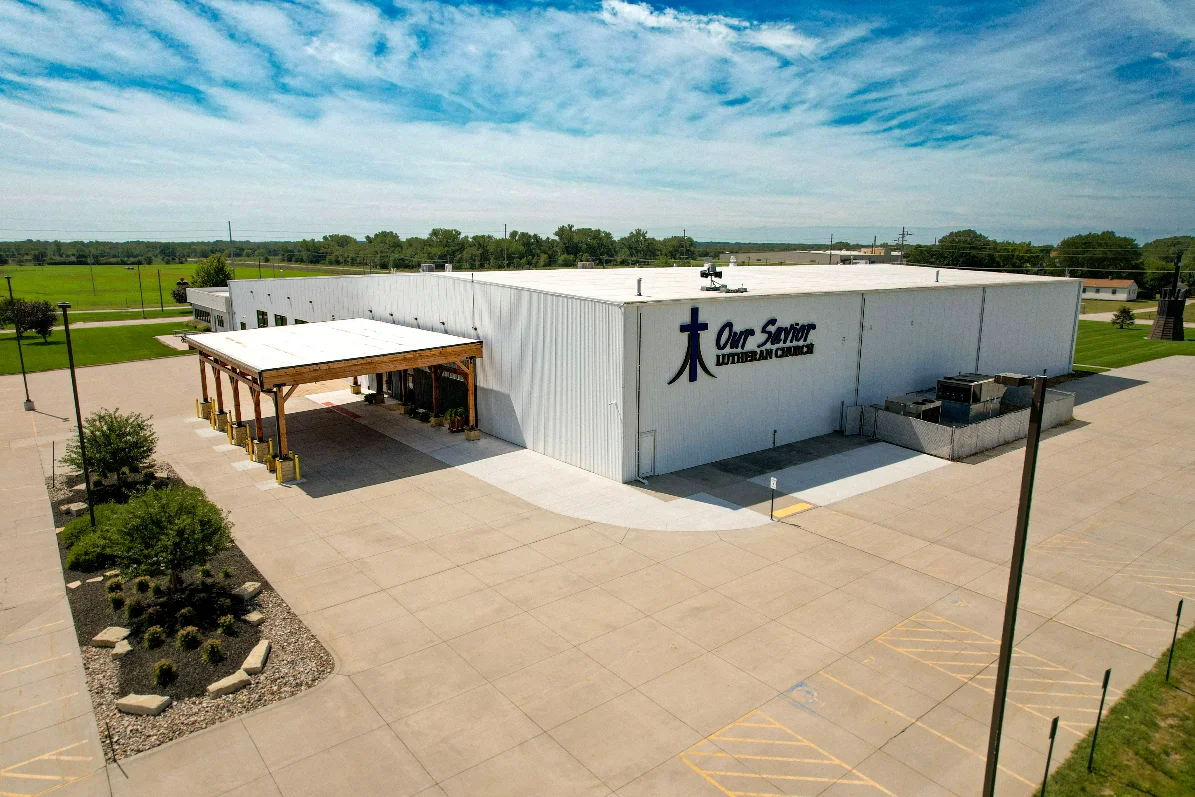 Aerial view of Our Savior Lutheran Church building with parking lot and green fields nearby.