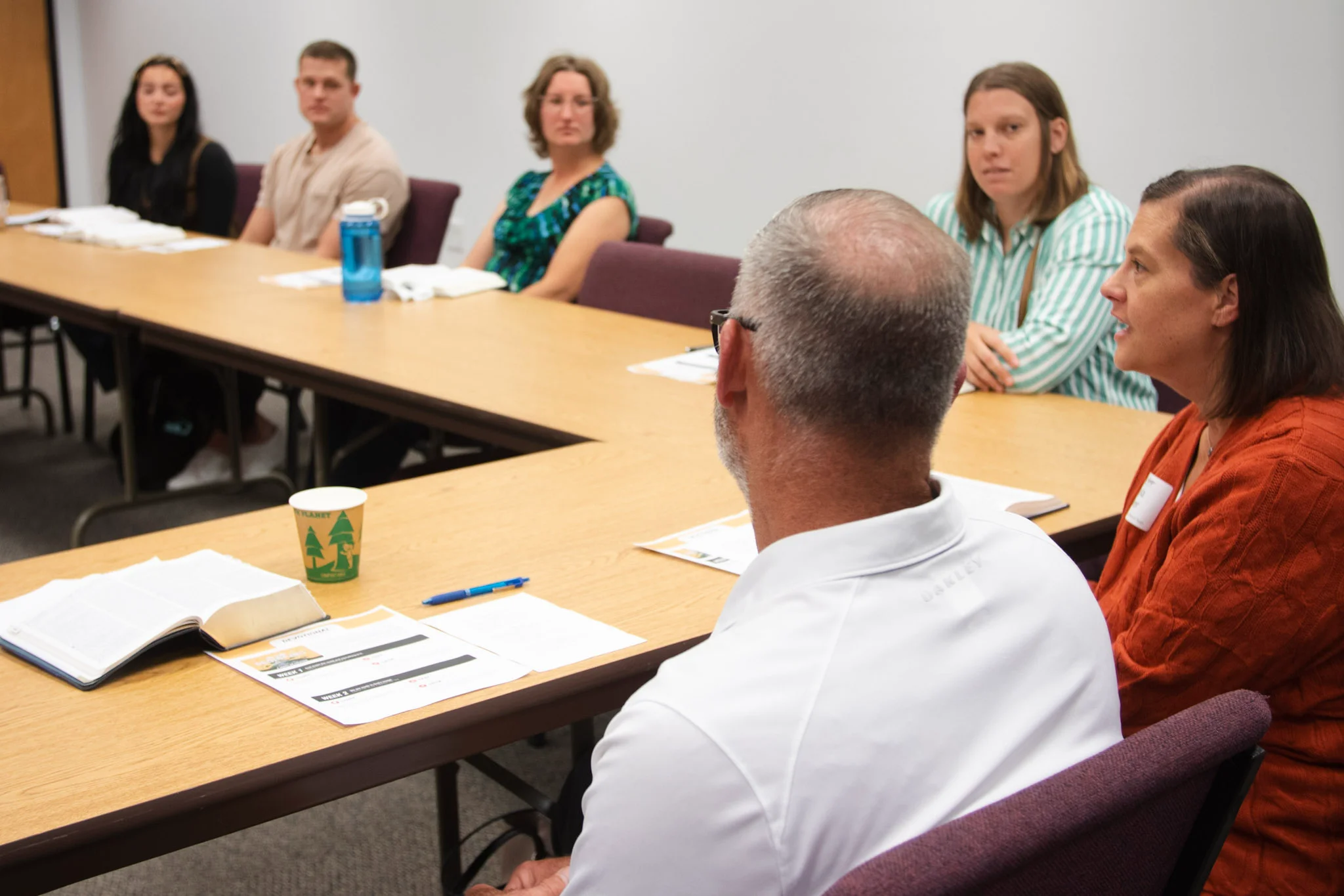 Group of six adults seated around a conference table engaged in a meeting or discussion.