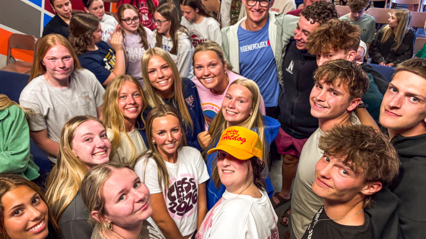 Large group of smiling teens gathered closely, some looking at the camera for a group selfie.
