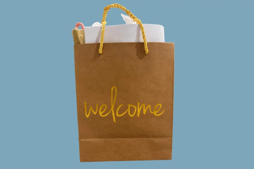 Brown paper gift bag with yellow rope handles and 'welcome' text, containing tissue paper and items.