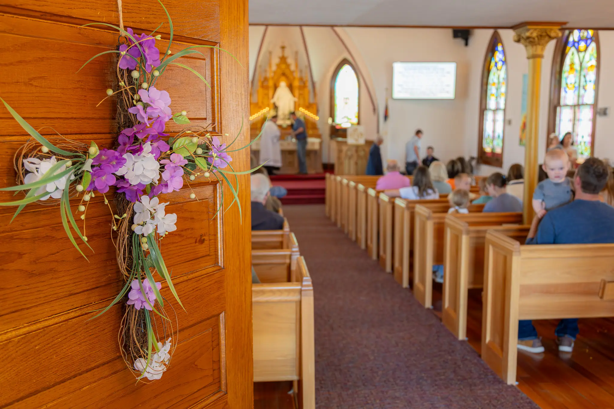 Floral cross on a pew end in a traditional sanctuary as the congregation worships.