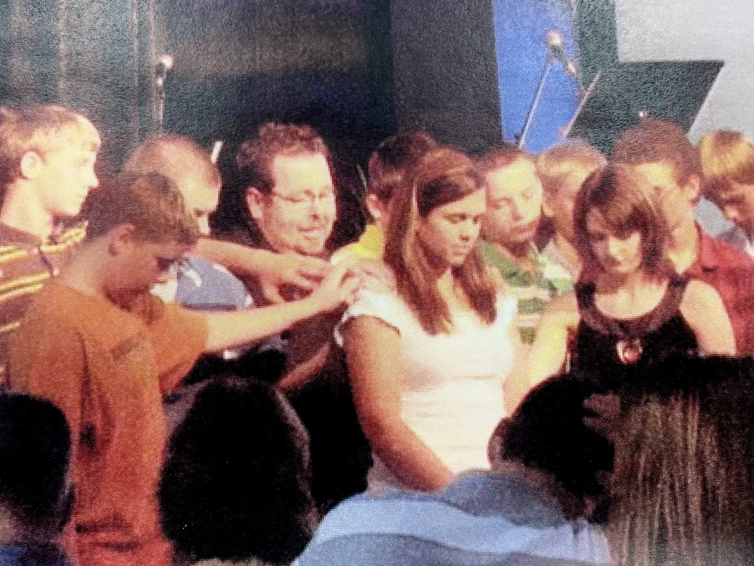 Group of teens pray together with bowed heads and hands laid on one another.