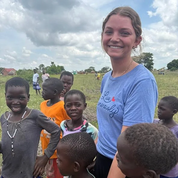 Smiling young woman surrounded by local children in a field during the Uganda mission trip.