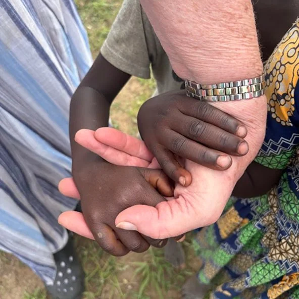 Close-up of an adult and a child holding hands during the Uganda mission trip.
