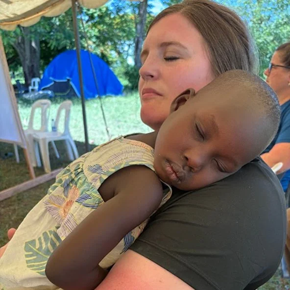 Woman cradles a sleeping child against her shoulder under a tent during the Uganda mission.