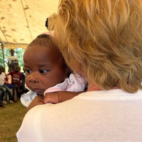 Woman holds a baby on her shoulder under a tent during the Uganda mission outreach.