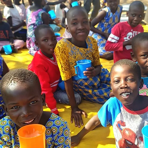 Children sit on a mat sharing drinks and a meal during the Uganda mission outreach.