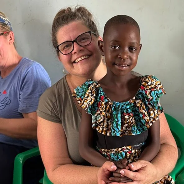 Smiling volunteer holds a young girl on her lap during the Uganda mission trip.