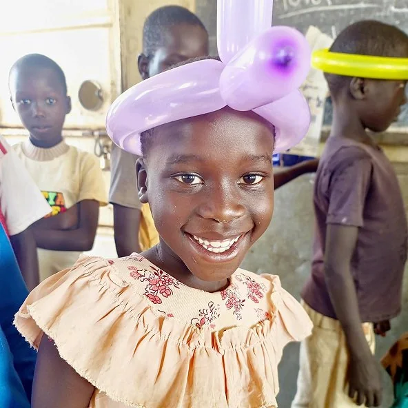 Smiling girl wears a purple balloon hat during the Uganda mission trip.